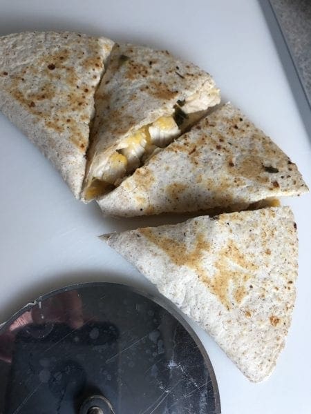 cut chicken quesadillas with a pizza cutter on a cutting board.